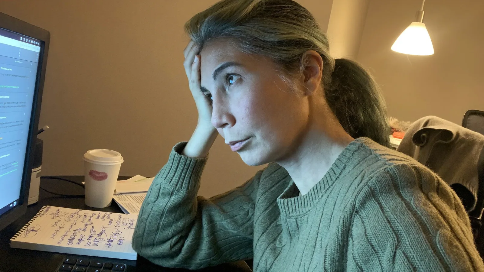 En kvinde ved sit skrivebord midt på formiddagen med fingrene presset mod tindingen